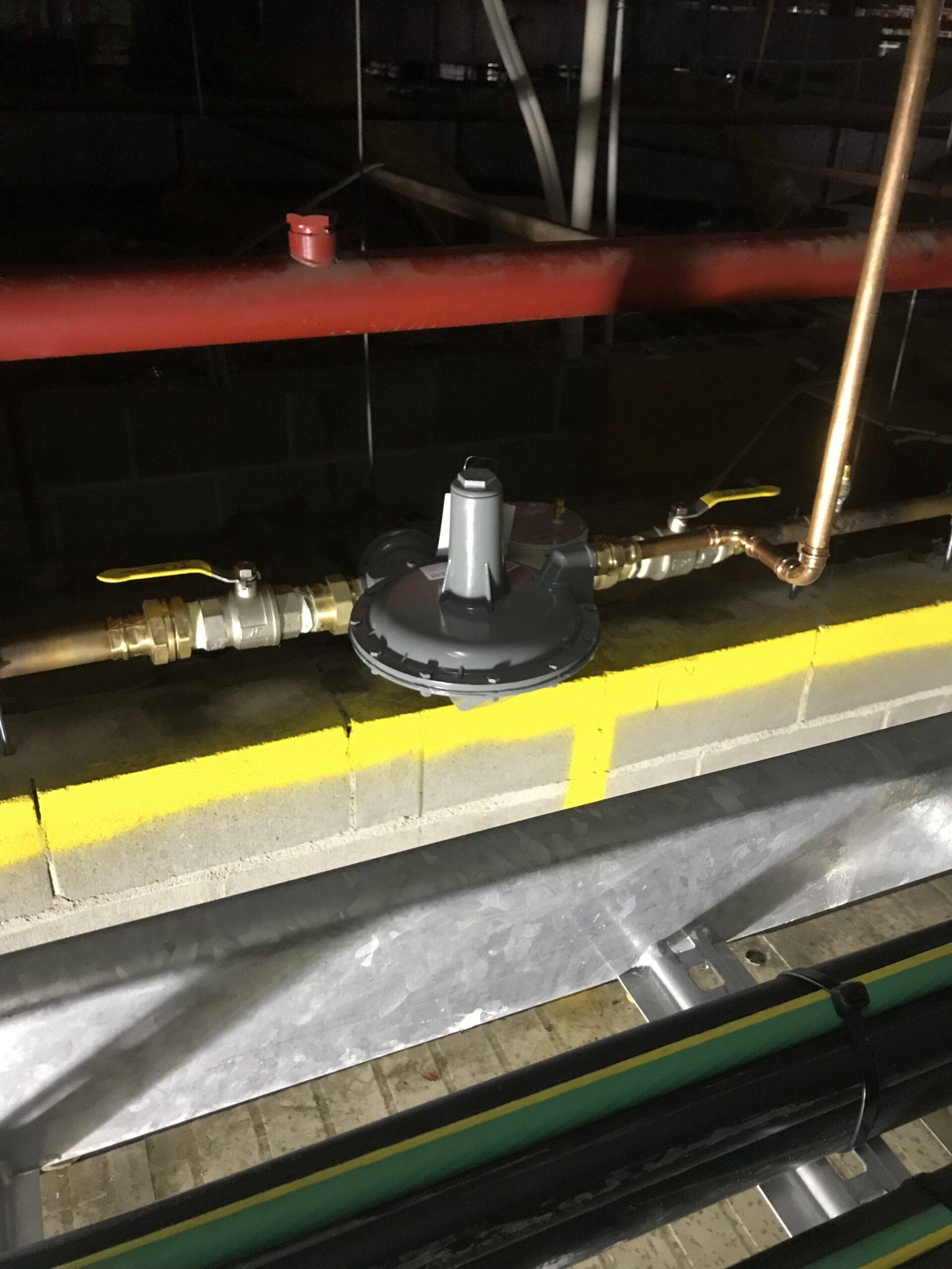 Industrial gas regulator installation with yellow safety markings and piping connections